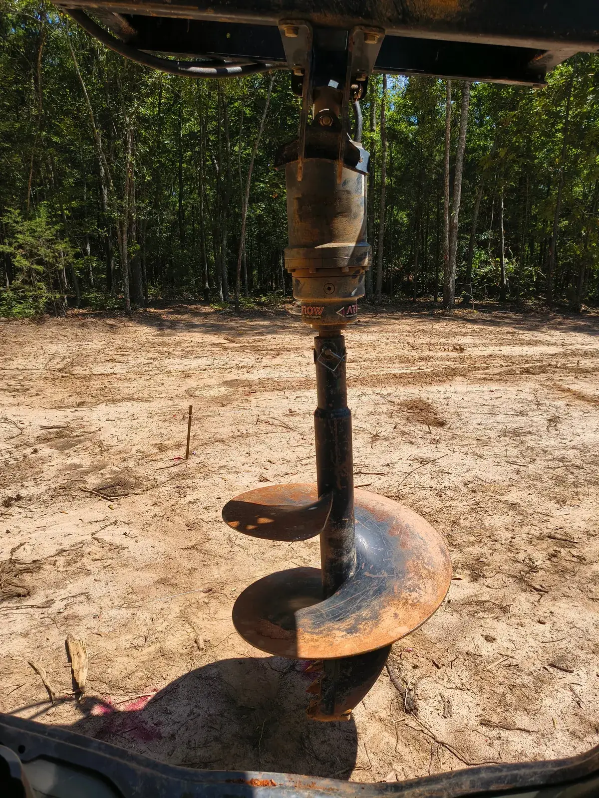 Skid steer auger attachment drilling a footer hole at a staked location