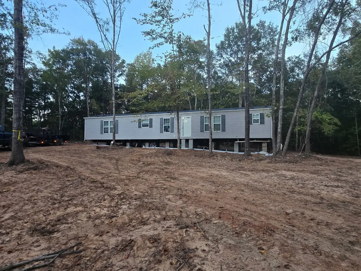 Gray mobile home set on the graded pad surrounded by trees