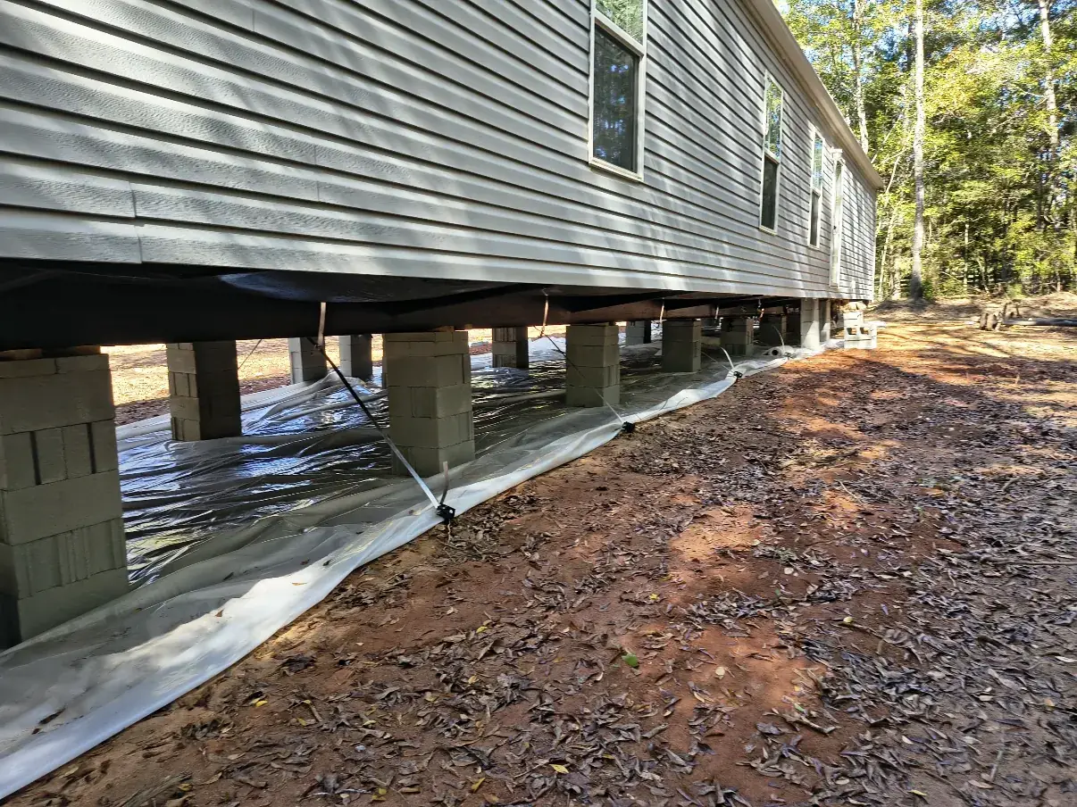 Low view along the underside of a mobile home showing block piers and ground moisture barrier